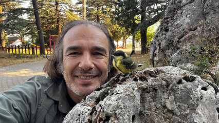 A man smiling as he takes a selfie with a cute titmouse perched on a rock in nature. © TAMER YILMAZ