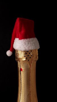 Champagne bottle wearing Santa Claus hat rotating on black background. New Year celebration. Vertical footage