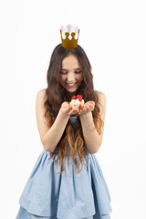 Cheerful young girl wearing crown blowing confetti from her hands in the studio