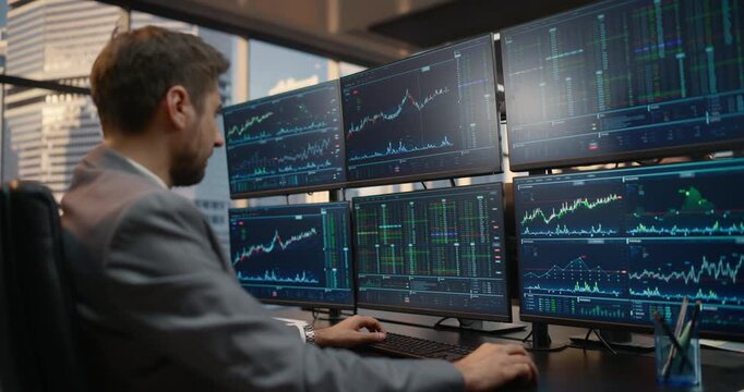 Profile Portrait of a Male Stockbroker Seated at a Desk With Six Monitors, Monitoring Financial Dashboards, Candlestick Charts and Ticker Data to Strategize Investments and Drive Capital Growth.