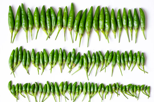 Organized horizontal rows of fresh green bird's eye chilies or cabe rawit hijau on white background