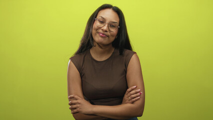 Obraz premium Woman, young brunette wearing glasses and brown sleeveless top, smiles and gives thumbs up while her arms are folded in studio; approval confidence.