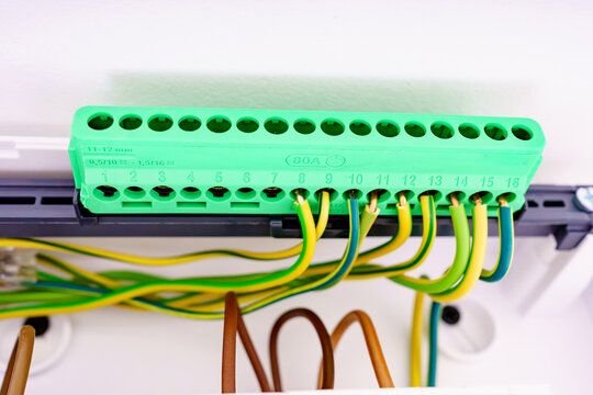 Closeup of a green grounding terminal block in an electrical panel. Modern brass busbar with connected yellow and green earth wires for home electrical safety and grounding.