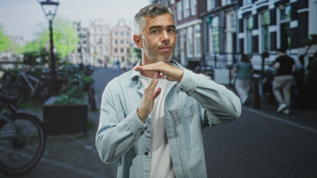 Man makes timeout t gesture with hands on city street, light blue jacket and stubble visible; thoughtful restraint.