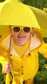 A happy child plays outside in an autumn park. A child with a yellow umbrella enjoys the autumn rain. Vertical video