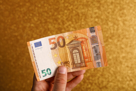 Close-up of a fifty euro note being held against a sparkling gold surface
