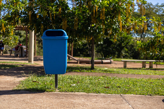 Cesto de lixo azul em parque p&uacute;blico arborizado e ensolarado / Blue trash can in a sunny, wooded public park