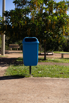 Cesto de lixo azul em parque p&uacute;blico arborizado e ensolarado / Blue trash can in a sunny, wooded public park