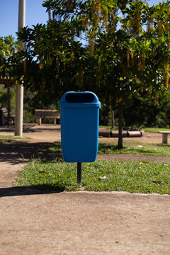 Cesto de lixo azul em parque p&uacute;blico arborizado e ensolarado / Blue trash can in a sunny, wooded public park