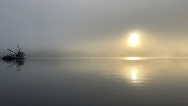 Fishing boat reflecting on foggy water with sunrise