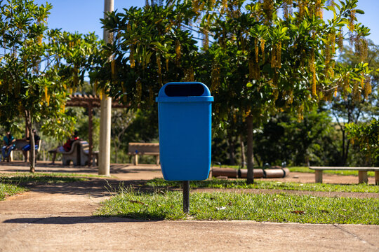 Cesto de lixo azul em parque p&uacute;blico arborizado e ensolarado / Blue trash can in a sunny, wooded public park
