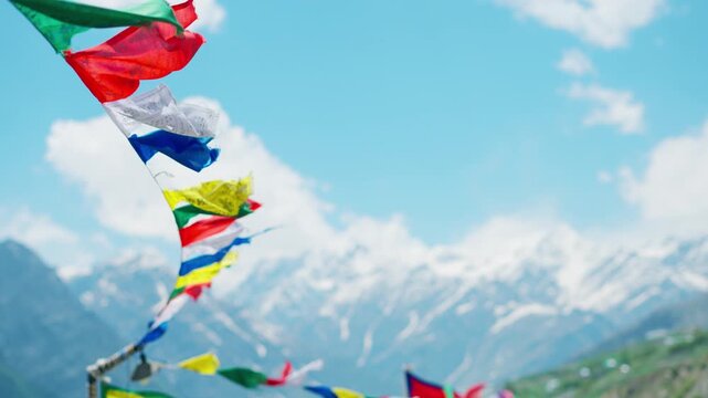 4K Slow motion shot of colorful Buddhist Tibetan prayer flags waving in the wind in front of snow covered Himalayan mountain peaks during the summer season at Lahaul Valley, Himachal Pradesh, India.