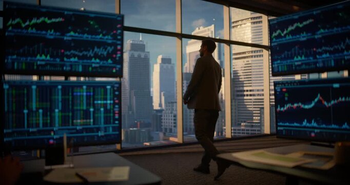 Tracking Shot Follows a Confident Businessman Walking Across a High-rise Office, Looking out of Windows on City Skyline as Trading Screens Show Live Market Data in Background
