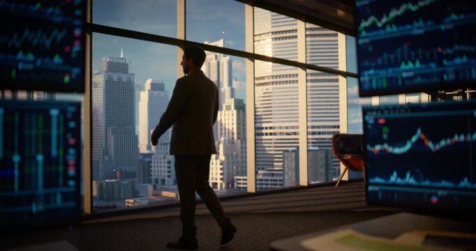 Thoughtful Caucasian Male CEO Standing at a High-rise Window, Planning Investment Decisions as Surrounding Monitors Show Live Stock Market Data and Charts. Cinematic Shot
