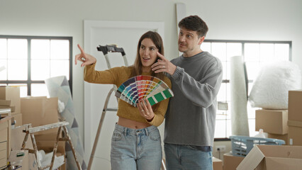 Fototapeta na wymiar Young woman and man holding a paint fan and pointing at color swatches in apartment living area; home renovation hopeful.