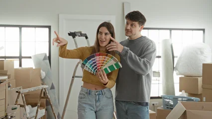 Young woman and man holding a paint fan and pointing at color swatches in apartment living area  home renovation hopeful. © Krakenimages.com