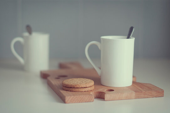 Close-up of Two mugs of tea and biscuits on a chopping board