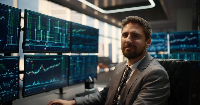 Portrait of Male Trader Turning and Looking at Camera while Working at Desk at Stock Exchange. Financial Graphs and Market Indices Shown Computer Screens,  Investing Success.