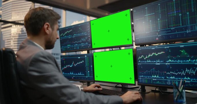 Male Trader Sits at Desk Reviewing Stock Exchange Data on Green Screen Chroma Key Monitors, Examining Financial Charts, Investment Analytics, Market Trends and Capital Growth in Office