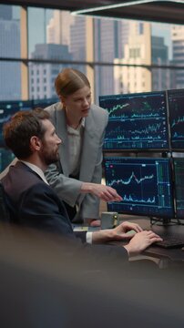 Vertical Screen. Two Brokers, a Man and Woman, Collaborate at a Desk, Pointing at Stock Market Data and Financial Charts, Discussing Trading Strategy and Investment Portfolio Growth as a Team.