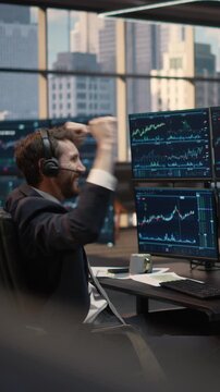 Vertical Screen. Portrait of Stockbroker Wearing Headset Celebrates Winning Trade at Desk, Analyzing Stock Market Data and Financial Charts, Reacting Joyfully to Successful Capital Growth Investment.