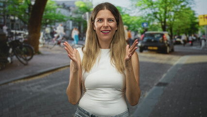 Fototapeta premium Woman hands clapping then wiping eyes on a busy street wearing white sleeveless top and jeans while smiling at camera; playful.