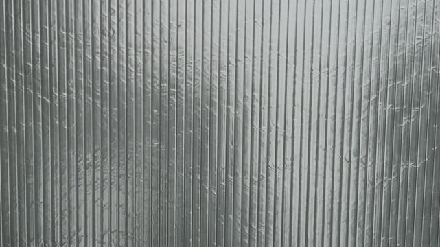 Translucent corrugated plastic panel viewed frontally with vertical ribbed structure, visible condensation, soft blurred shapes behind surface, muted gray tones, and clean industrial texture for
