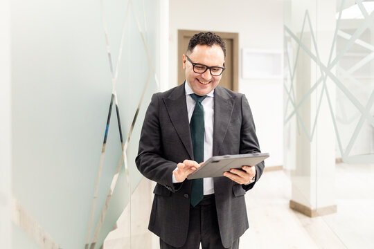 Medium shot of a lawyer or business professional, aged 40-50, in a suit, looking at a tablet in a modern office. Concept of mature businessmen.