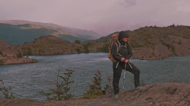 Standing female hiker with backpack experiencing the windy conditions of patagonia in front of a rocky landscape, Torres del Paine, Patagonia