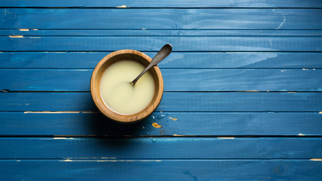 Top view of condensed milk in wooden bowl on blue wooden background