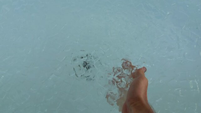 Hand Holds Ice Cubes Over a Bathtub Filled With Cold Water, Preparing Cryotherapy for Muscle Recovery, Endurance and Healthy Lifestyle