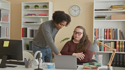 Man points to laptop and shows papers while seated woman watches with folded arms in an office workspace with bookshelves and a clock  mentoring focus. © Krakenimages.com