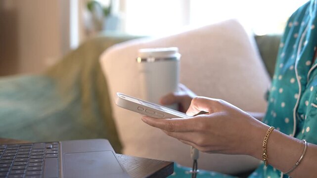 Person using smartphone and laptop while drinking coffee at home. Morning remote work,mobile communication, AI workflow,digital productivity,email management,cloud collaboration, hybrid work lifestyle