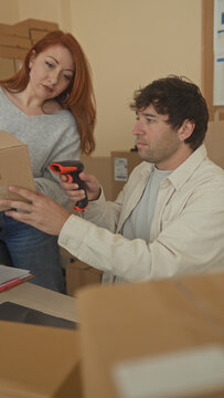 Man and woman pack and scan multiple cardboard parcels at a laptop and handheld scanner in a small shipping area inside a building; focused teamwork.