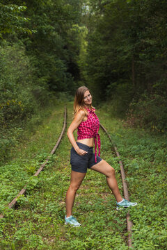 Woman in plaid shirt posing on an abandoned railway track in a green forest. Lifestyle portrait of travel, adventure, hiking and freedom concept
