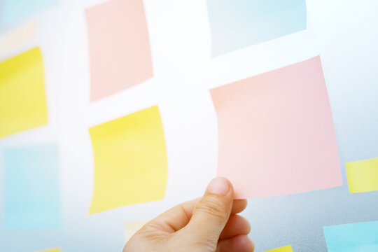 close up hand people business man post it notes in the wall at meeting room. Sticky note paper reminder schedule board. Colorful variety copy empty space. soft focus.