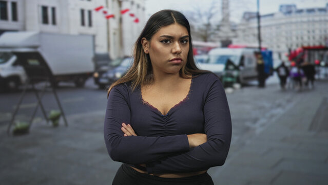 Woman with arms crossed and stern expression on a city street in navy vneck longsleeve shirt; frustration defiance.