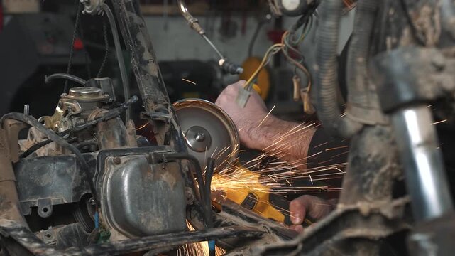 An engineer in a garage is modifying a motorcycle, sawing and trimming off excess frame elements with a circular saw.
