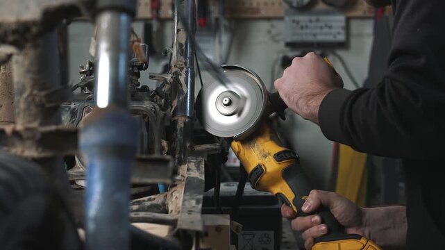 An engineer in a garage is modifying a motorcycle, sawing and trimming off excess frame elements with a circular saw.