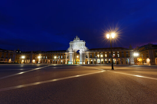 Magnificent blue-hour view of the Comercio square in Lisbon, with the iconic Arco da Rua Augusta brilliantly illuminated at the far end of the grand yellow arcaded square.