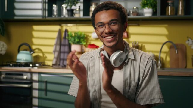 Happy African American male student clapping hands at home kitchen looking at camera smiling guy applauding support while studying homework writing notes at table freelancer education success praise