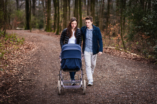 Ein junges Paar schiebt einen Kinderwagen auf einem Waldweg, KI generiert