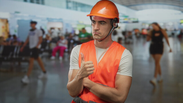 Man in orange safety vest and hardhat gives thumbs up with a puzzled expression in a busy airport terminal; doubt reluctant approval.