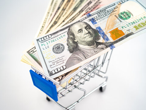 Close up of miniature shopping cart filled with US dollar banknotes isolated on white background