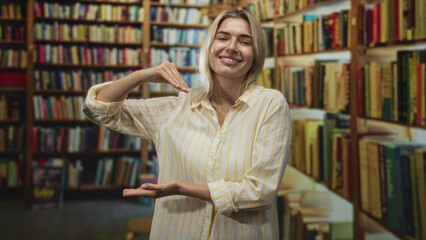 Woman holds one hand above her other palm while smiling beside crowded bookshelves in a cozy library  playful curiosity warmth. © Krakenimages.com