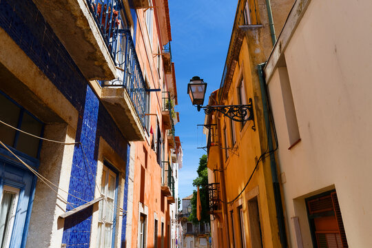 Vivid narrow street in Lisbon's Mouraria district featuring a building covered in deep blue azulejo tilework beside warm orange and ochre rendered facades.