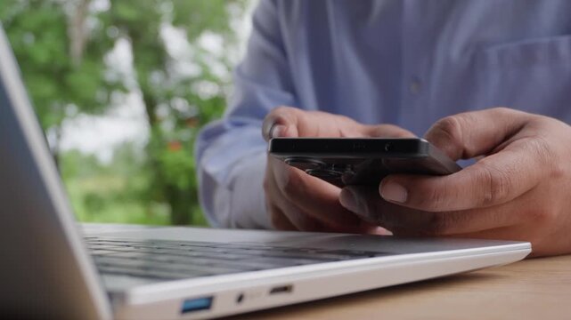 Business professional using smartphone while working on laptop at modern workspace, representing mobile communication, digital workflow, remote productivity, business technology, connected workplace