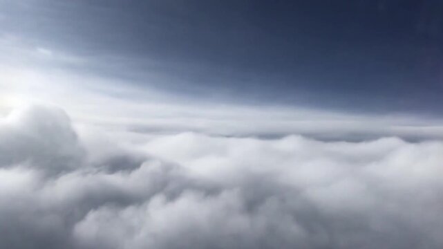 A point-of-view (POV) shot from an airplane window or high altitude, revealing a stunning contrast between the whiteness of cumulus clouds and the serene blue sky gradations above.