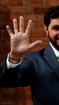 Showing numbers using fingers with confident expression, Indian Asian bearded ceo businessman in formal corporate attire demonstrating finger counting while standing in cozy office against brick wall