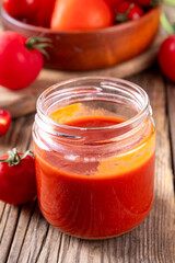 Homemade tomato paste, puree, sauce or ketchup in a small glass jar. Tasty tomato preserves from fresh ripe red tomatoes, on a wooden background with fresh vegetables © ricka_kinamoto